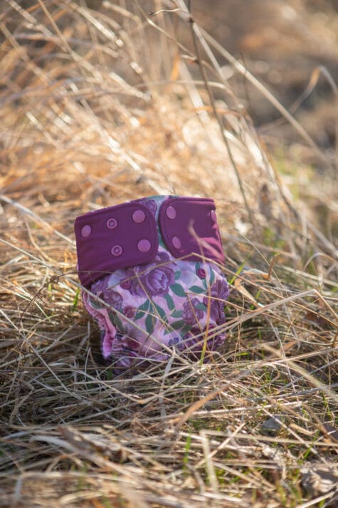 en lila och rosa tygblöja med motiv av blommor som ligger i gräset