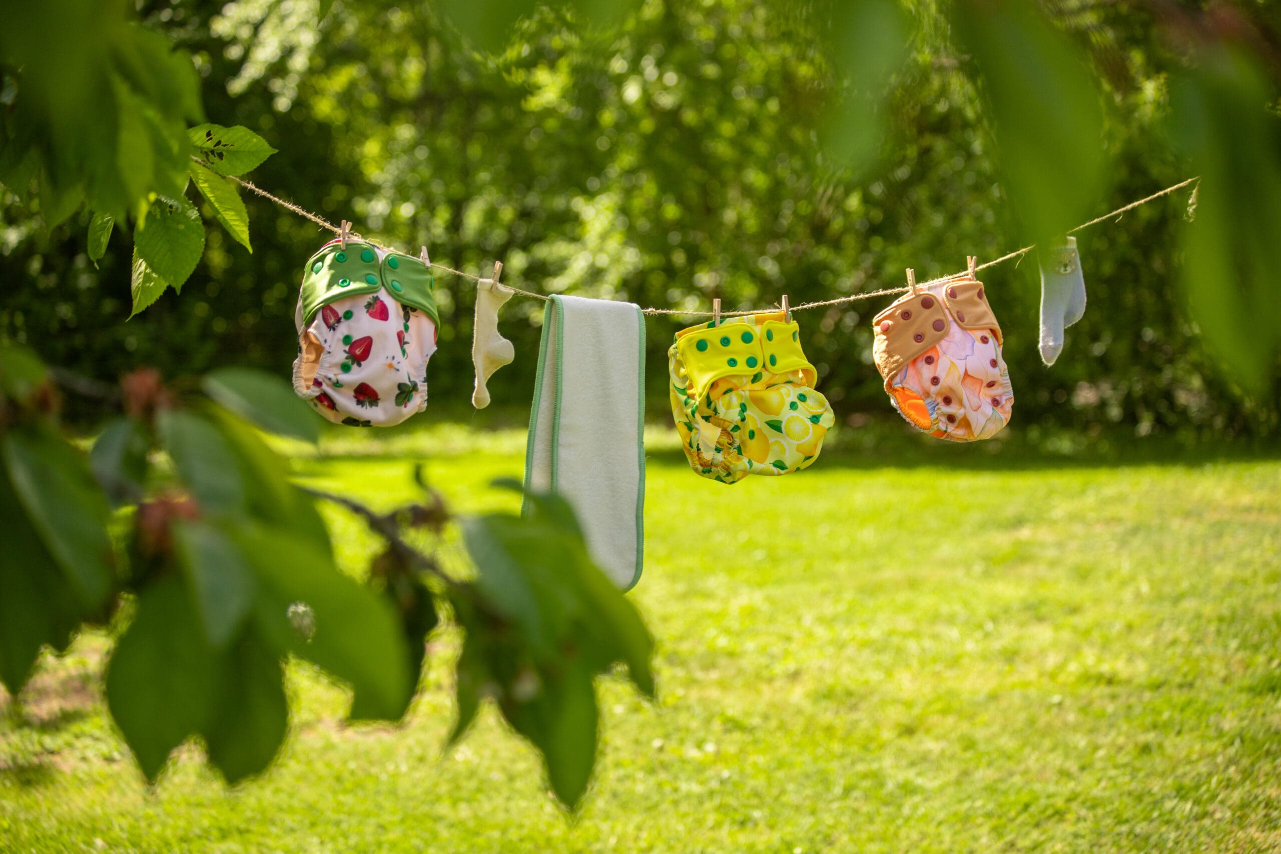 tygblöjor och inlägg som hänger på en lina utomhus och torkar. det är sommar och bakgrunden är gräs